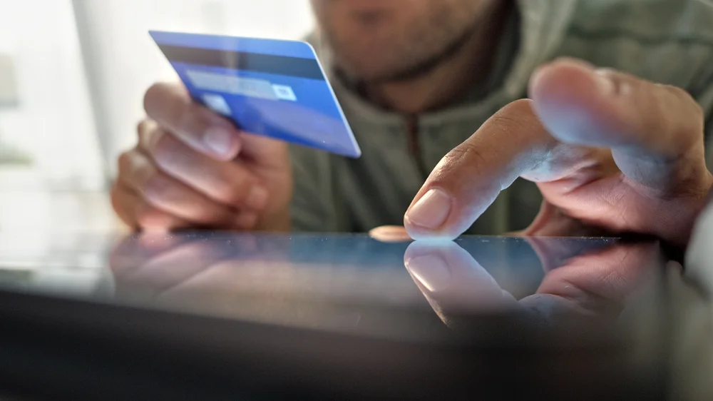 Close up of a man holding a credit card and entering payment info on a tablet