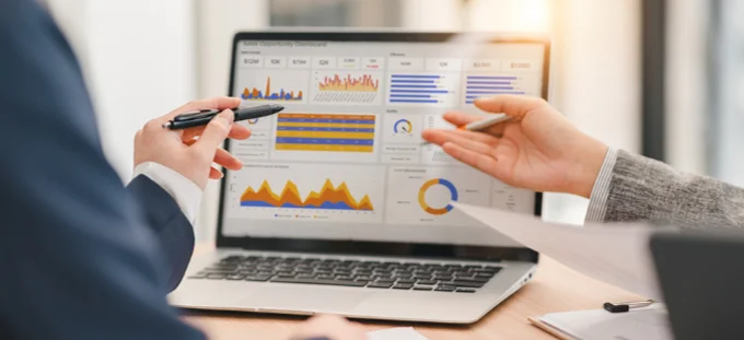 Close of a laptop screen displaying financial charts and data with the hands of two colleagues gesturing towards the data
